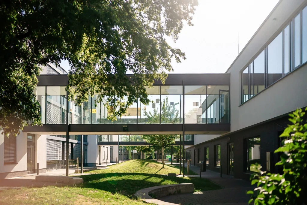 Blick durch einen begrünten Innenhof mit Glasbrücken zwischen modernen Bürogebäuden.