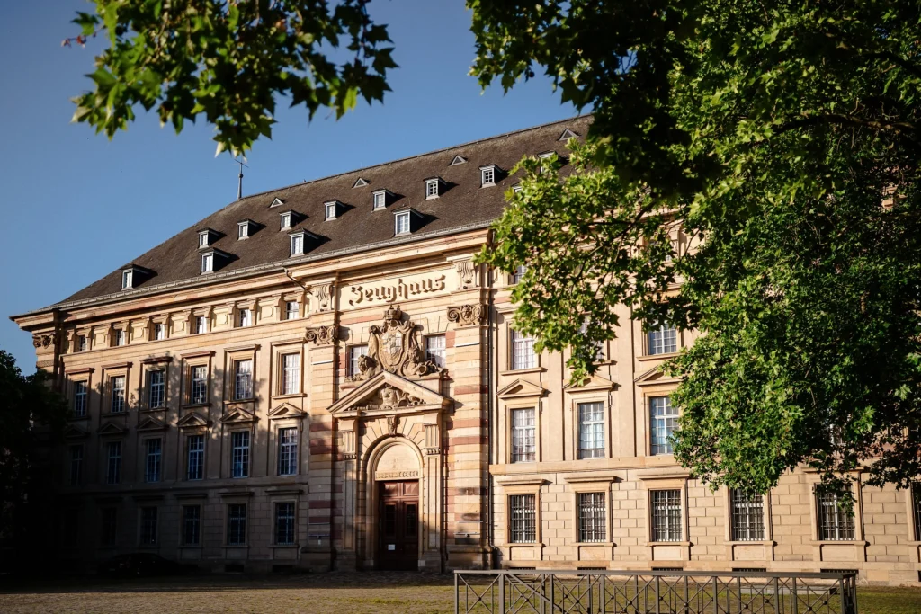 Das historische Zeughaus mit seiner verzierten Sandsteinfassade steht hinter einer freien Platzfläche und wird von Bäumen eingerahmt.