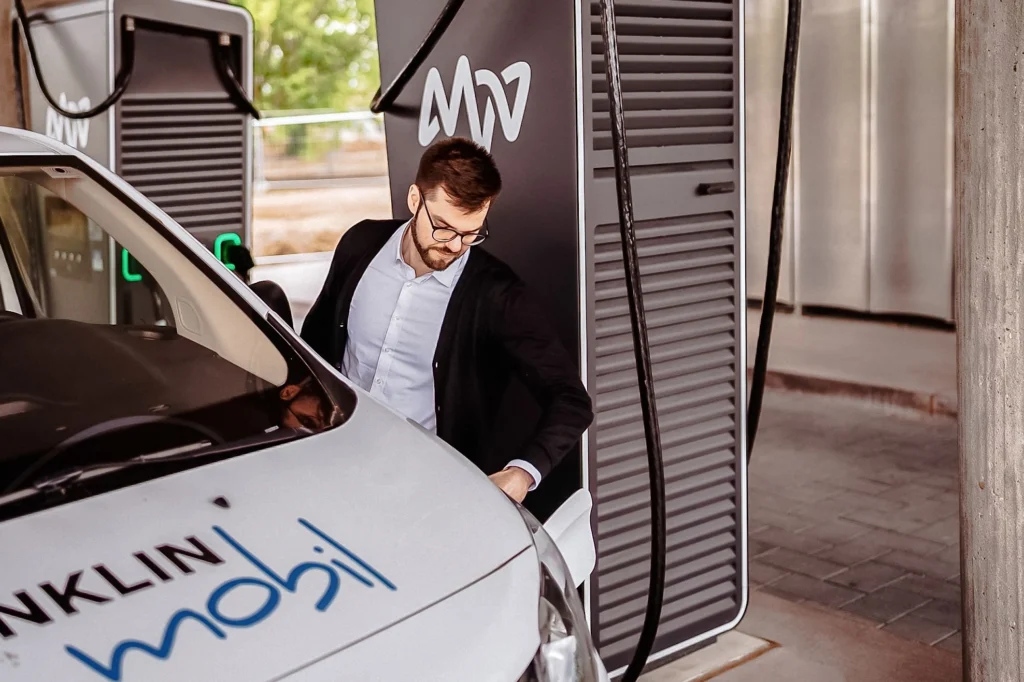 Mann mit Brille lädt Elektroauto an Ladestation mit Aufschrift MVV auf.