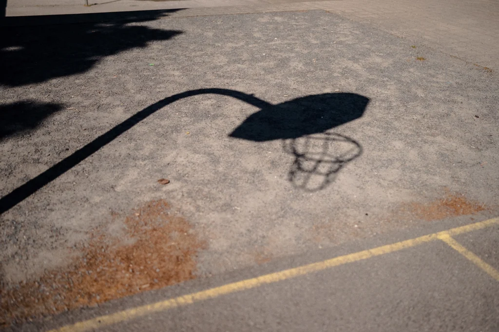 Schatten eines Basketballkorbs auf einem Sportplatz.