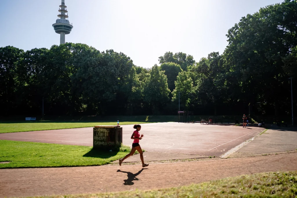 Eine Person joggt an einer Sportanlage vorbei, während im Hintergrund Bäume und der Fernmeldeturm zu sehen sind.