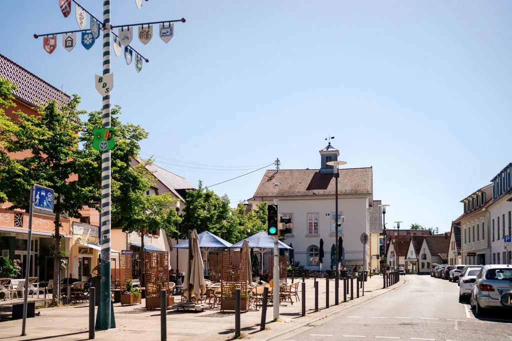 Dorfplatz in Wallstadt mit Maibaum, Außengastronomie und historischen Gebäuden.