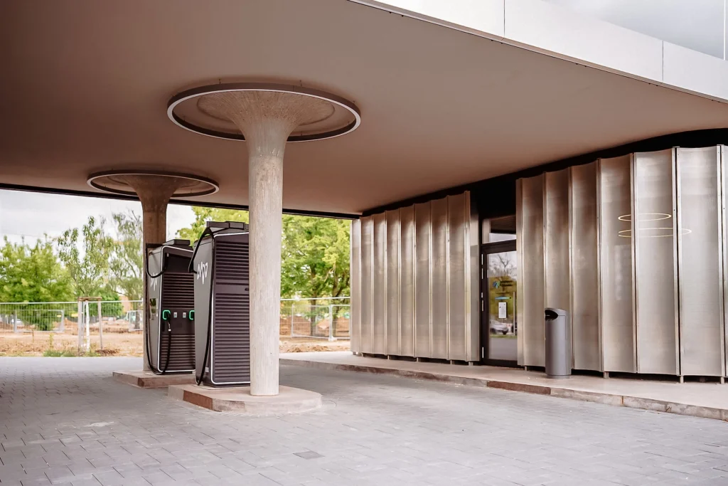 Eine überdachte Ladestation für Elektrofahrzeuge befindet sich vor einem modernen Gebäude.