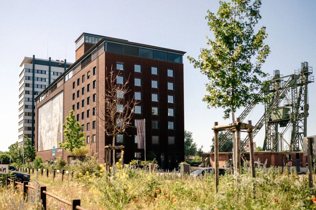 Mehrstöckiges Backsteingebäude im Jungbusch Mannheim mit Bäumen und Industrieanlagen im Vordergrund.