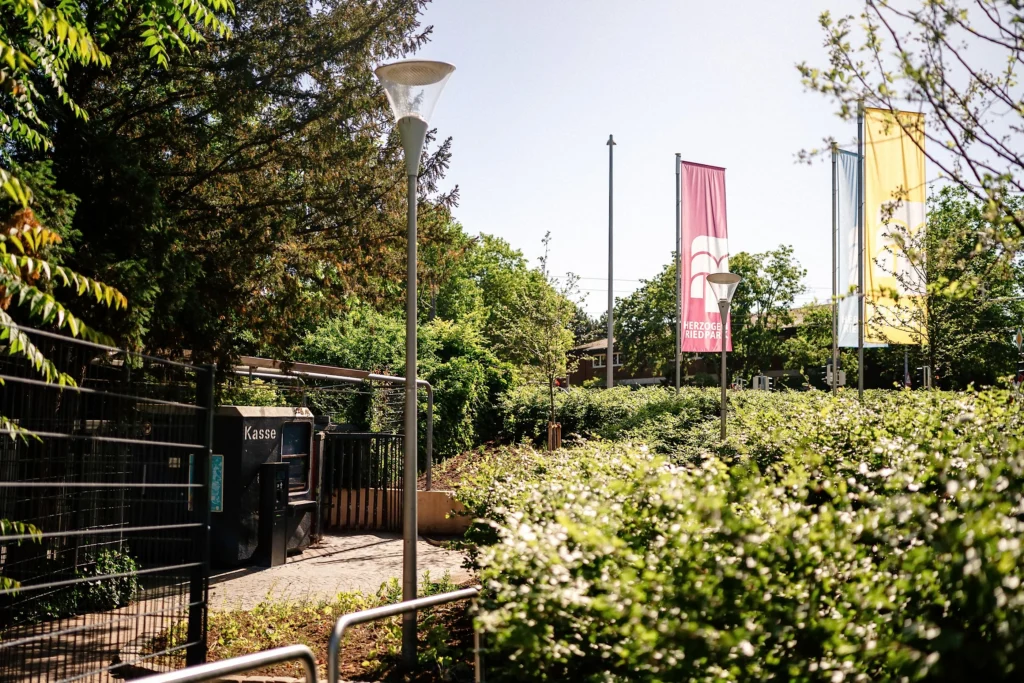 Der Eingangsbereich vom Herzogenriedpark mit Fahnen, Laternen und Hecken.