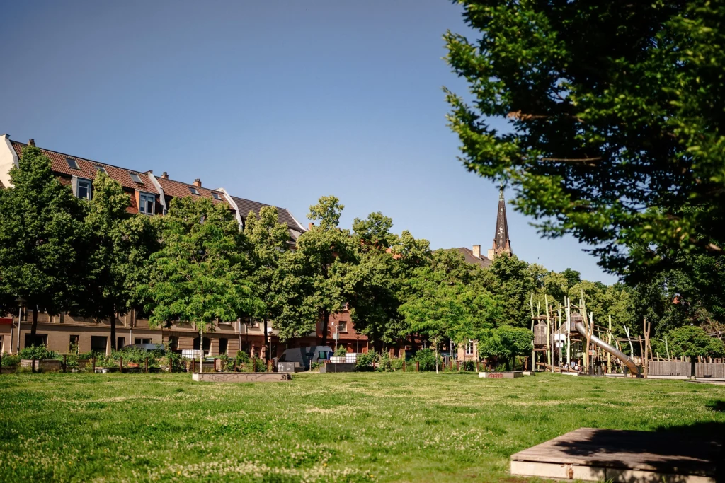 Große Grünfläche mit Spielplatz und Wohnhäusern im Hintergrund.