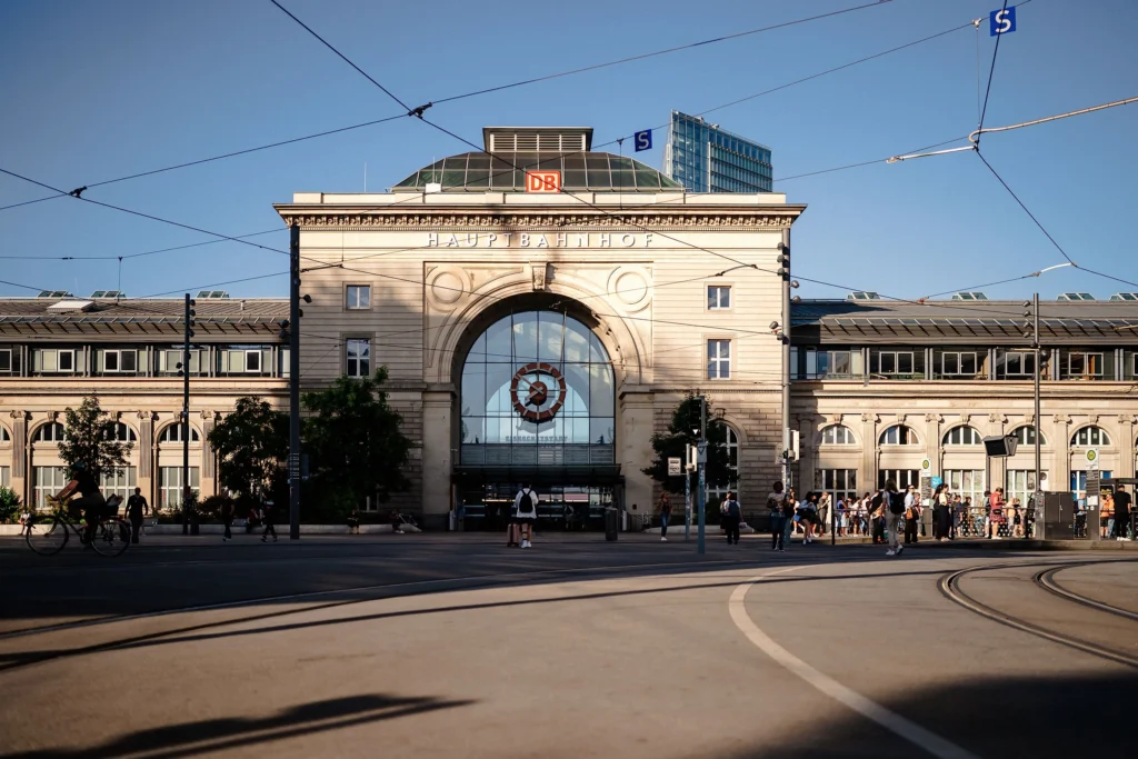 Die historische Fassade des Mannheimer Hauptbahnhofs mit dem großen Eingangsportal liegt vor Straßenbahngleisen und einem Bahnhofsvorplatz.