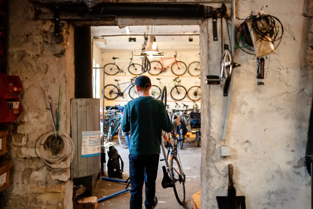 Ein Mitarbeiter schiebt ein Fahrrad durch den Eingang einer Fahrradwerkstatt mit zahlreichen ausgestellten Fahrrädern.
