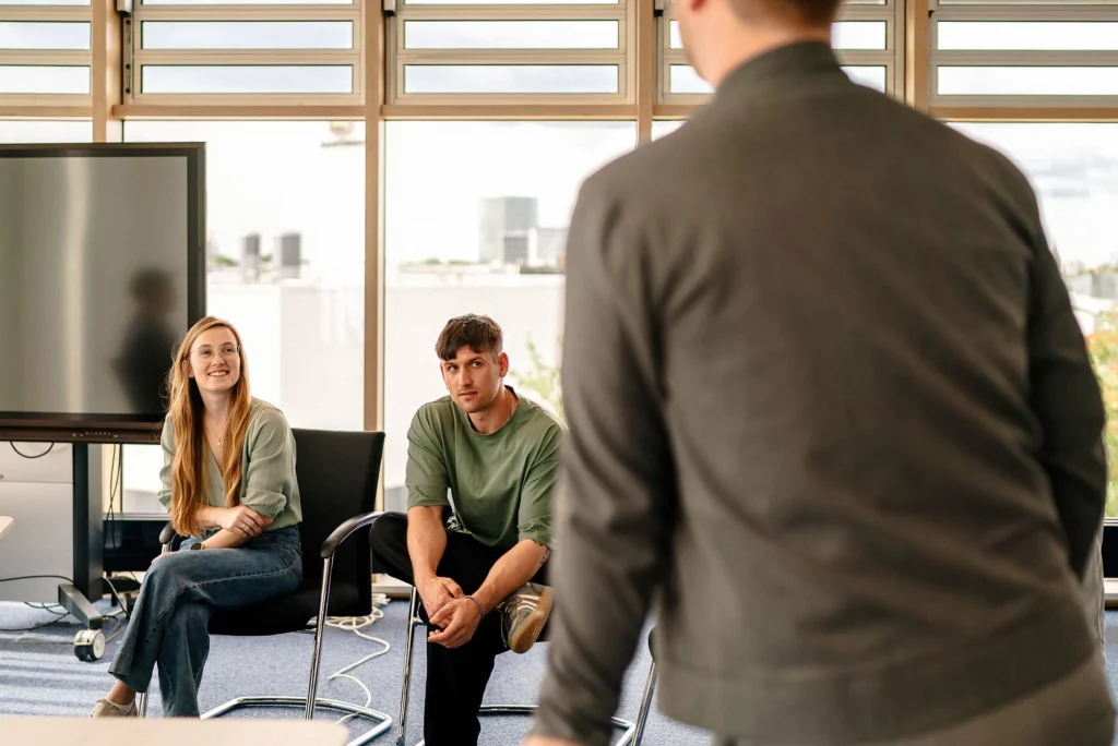 Mehrere Personen sitzen in einem Besprechungsraum und hören einer Präsentation zu.