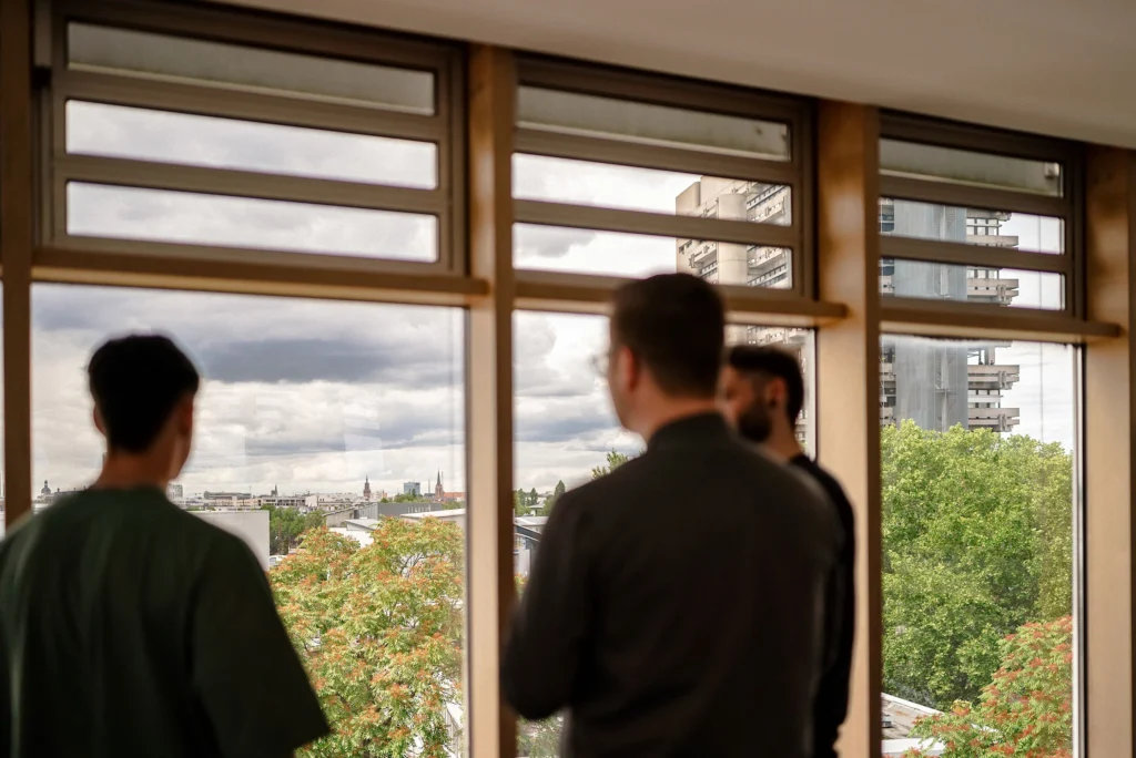 Mehrere Personen blicken durch große Fenster auf die Mannheimer Innenstadt und den Fernmeldeturm.