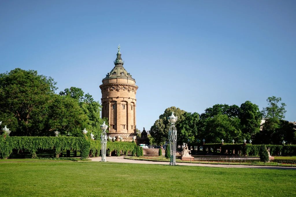 Der Mannheimer Wasserturm steht vor einer großen Rasenfläche und von Bäumen umgebenen Parkanlagen.