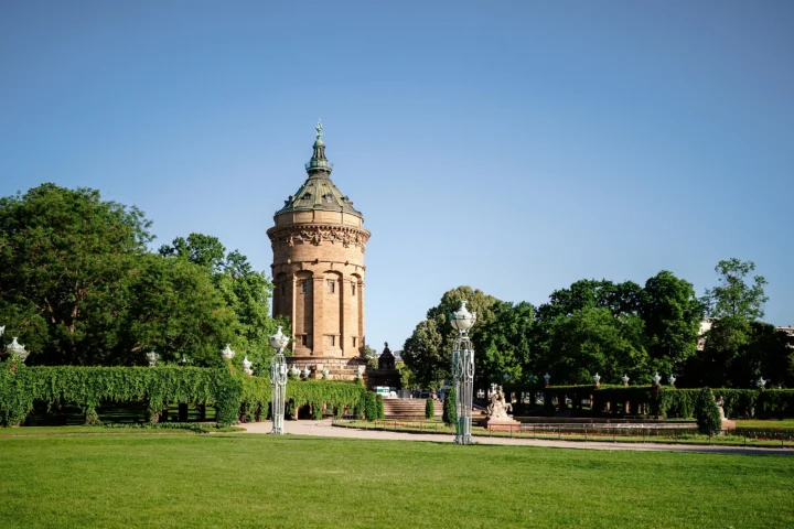 Der Mannheimer Wasserturm steht vor einer großen Rasenfläche und von Bäumen umgebenen Parkanlagen.