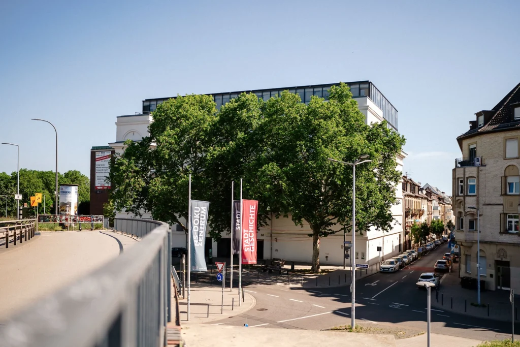 Eine Straßenkreuzung mit dem Gebäude des MARCHIVUM ist von Bäumen, Wohnhäusern und Straßen umgeben.