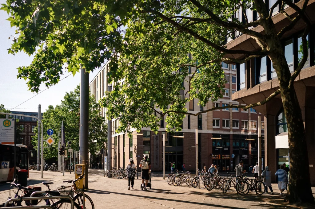 Stadtstraße mit Bäumen, Fahrradständern und mehreren Personen in Mannheim bei Tageslicht.