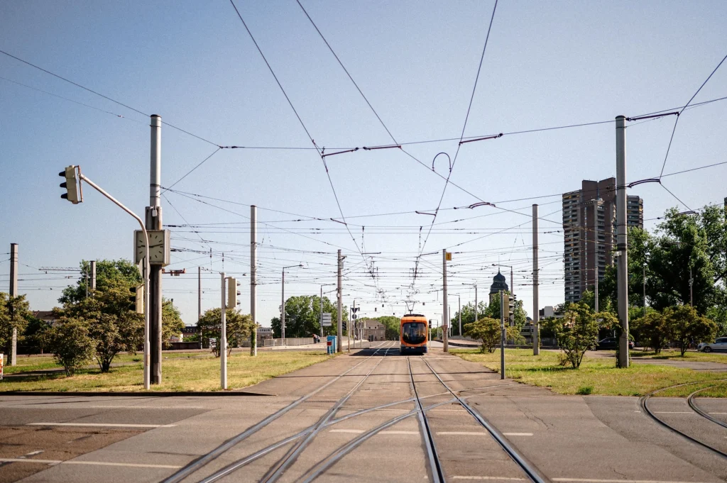 Blick auf eine Straßenbahn auf der Kurpfalzbrücke Mannheim mit Gleisen und Oberleitungen in einer offenen städtischen Umgebung.