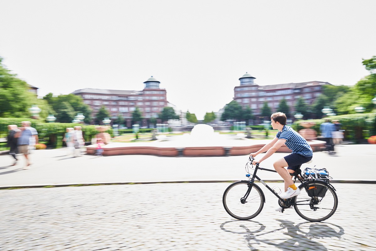 Ein Radfahrer genießt eine entspannte Fahrt am Wasserturm in Mannheim. Die grüne Umgebung und die historische Architektur bieten eine malerische Kulisse für Freizeitaktivitäten.