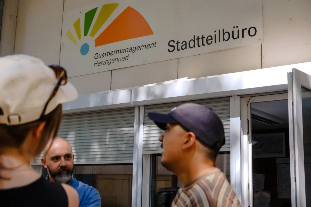 Several people stand in front of the Herzogenried neighborhood office and talk to each other.