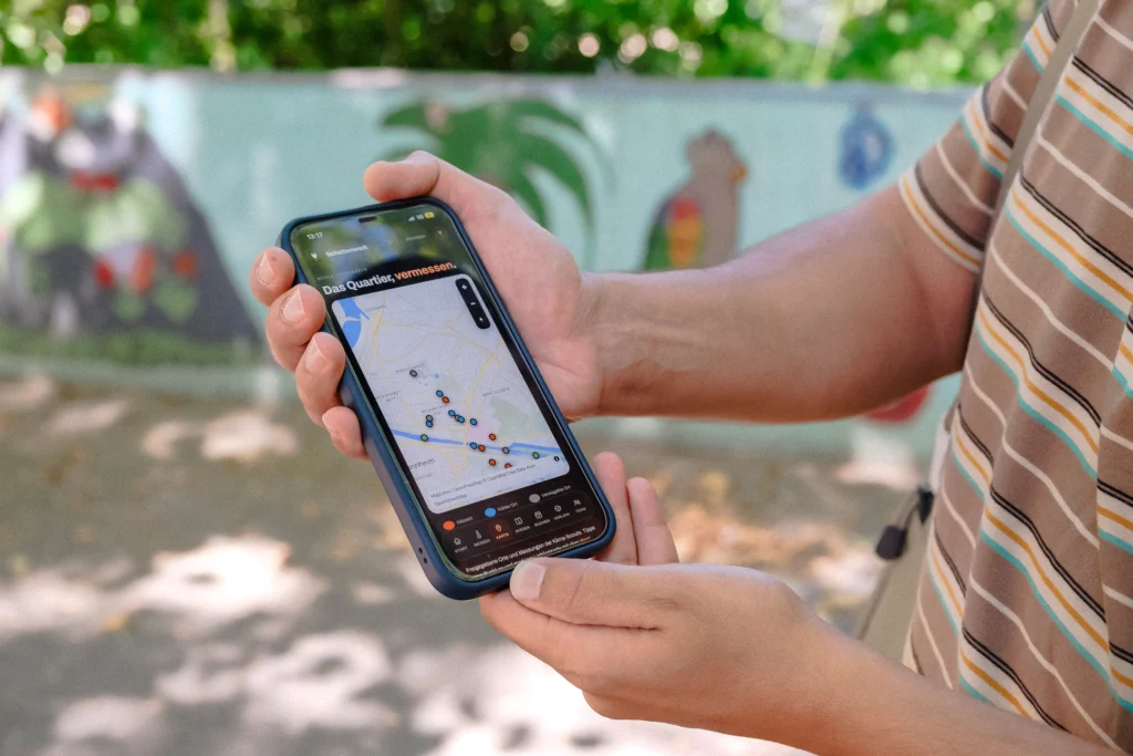 Eine Person zeigt auf einem Smartphone eine Karte mit markierten Messpunkten im Quartier.