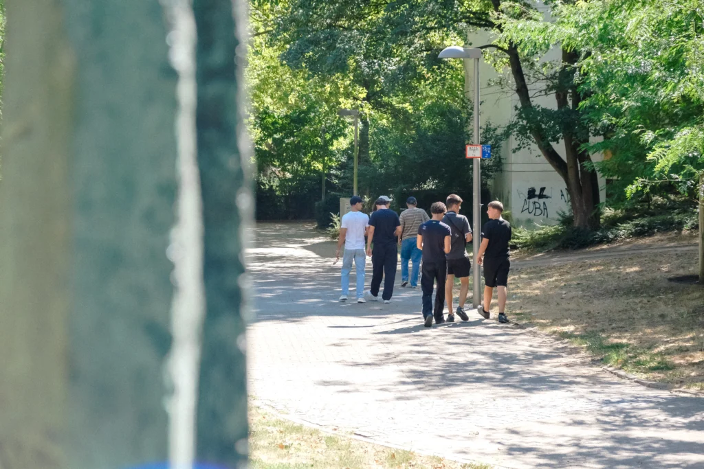 Eine Gruppe bewegt sich zu Fuß durch das Quartier auf einem breiten Weg zwischen Bäumen und Wohnhäusern