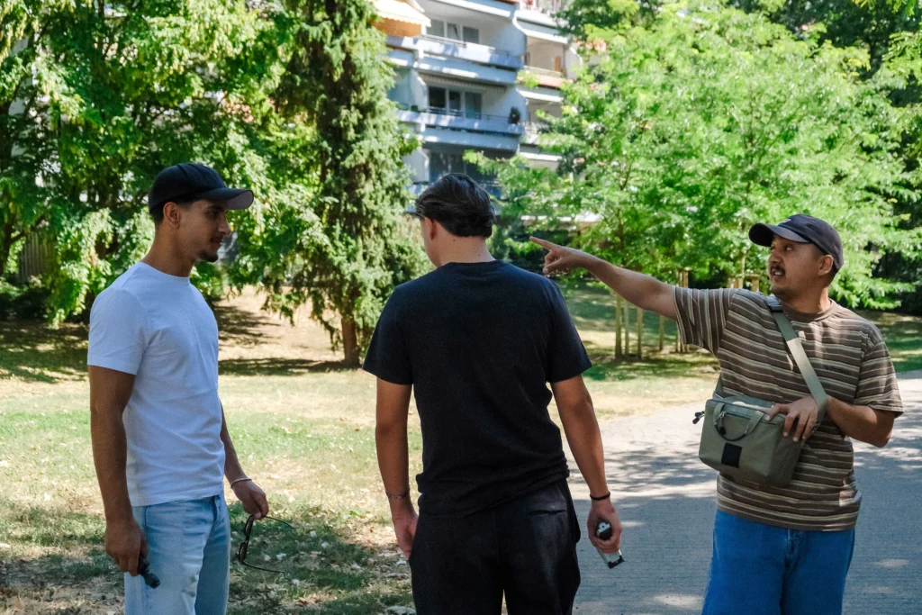 Eine Gruppe steht auf einem Weg im Grünen, während eine Person auf einen Bereich im Quartier zeigt und etwas erklärt.