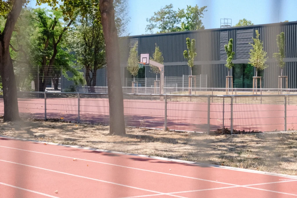 Sportanlage mit Laufbahn und Basketballkorb neben einem modernen Schulgebäude.