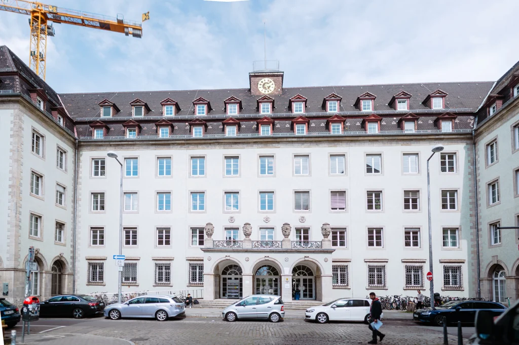 Historic building with a clock tower and central entrance along a street with parked cars in Mannheim.