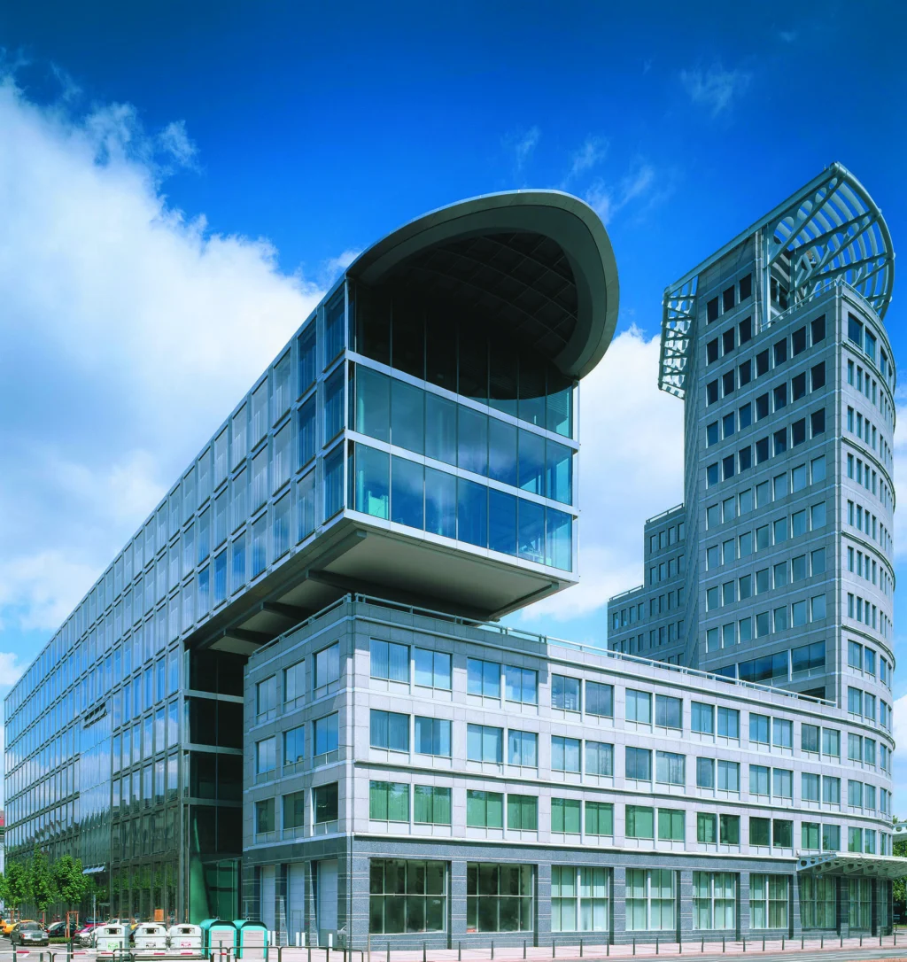 Bürogebäude der Mannheimer Versicherung mit moderner Glasfassade und markantem, abgerundetem Dach sowie angrenzendem hohen Turm mit Uhr