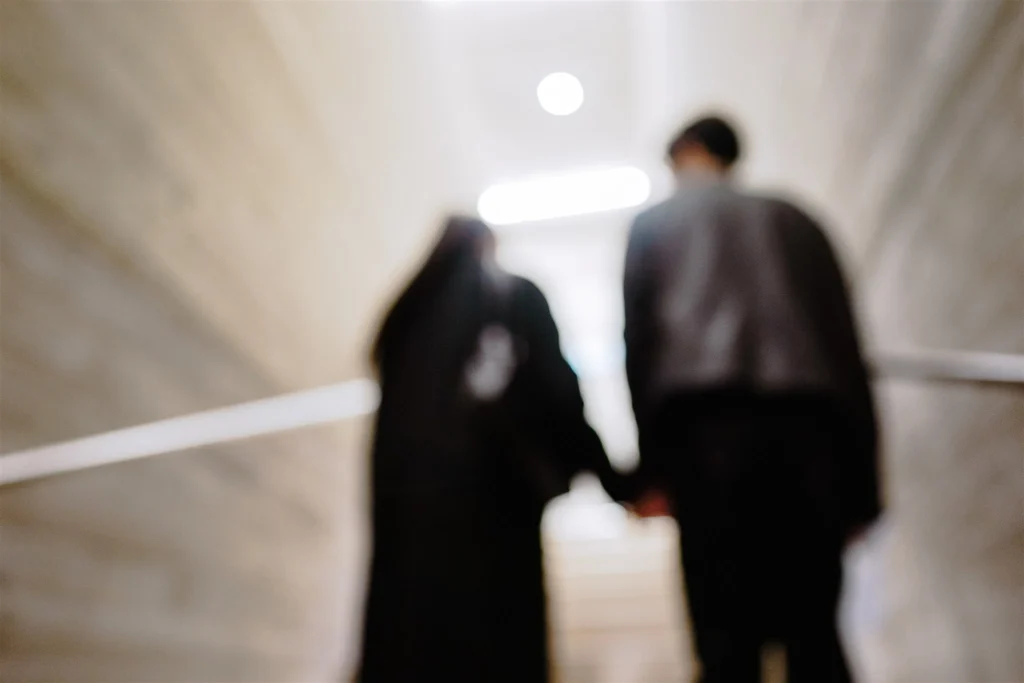 Zwei unscharfe Personen gehen Hand in Hand durch einen beleuchteten Gang.