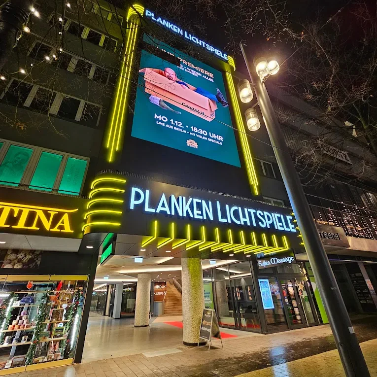 Fassade des Kinos Planken Lichtspiele Mannheim bei Nacht mit beleuchtetem Schriftzug und digitaler Anzeigetafel über dem Eingang.