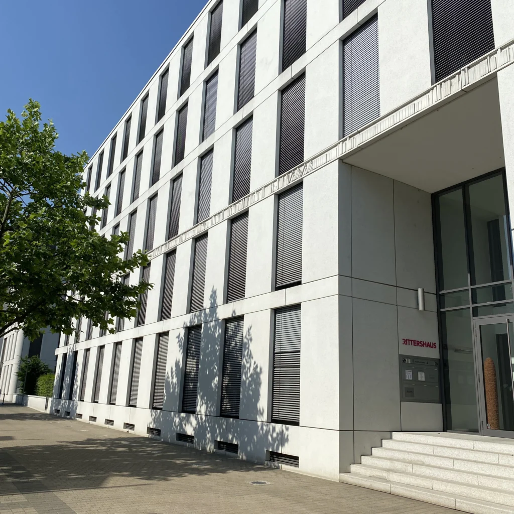 Modernes mehrstöckiges Bürogebäude mit rechteckigen Fenstern und Eingang mit Treppe, an der Wand steht RITTERSHAUS.