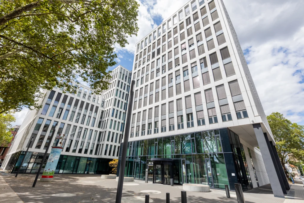 Moderne mehrstöckige Bürogebäude der Firma Südzucker mit weißer Fassade und großen Fenstern, umgeben von Bäumen und einem gepflasterten Vorplatz.