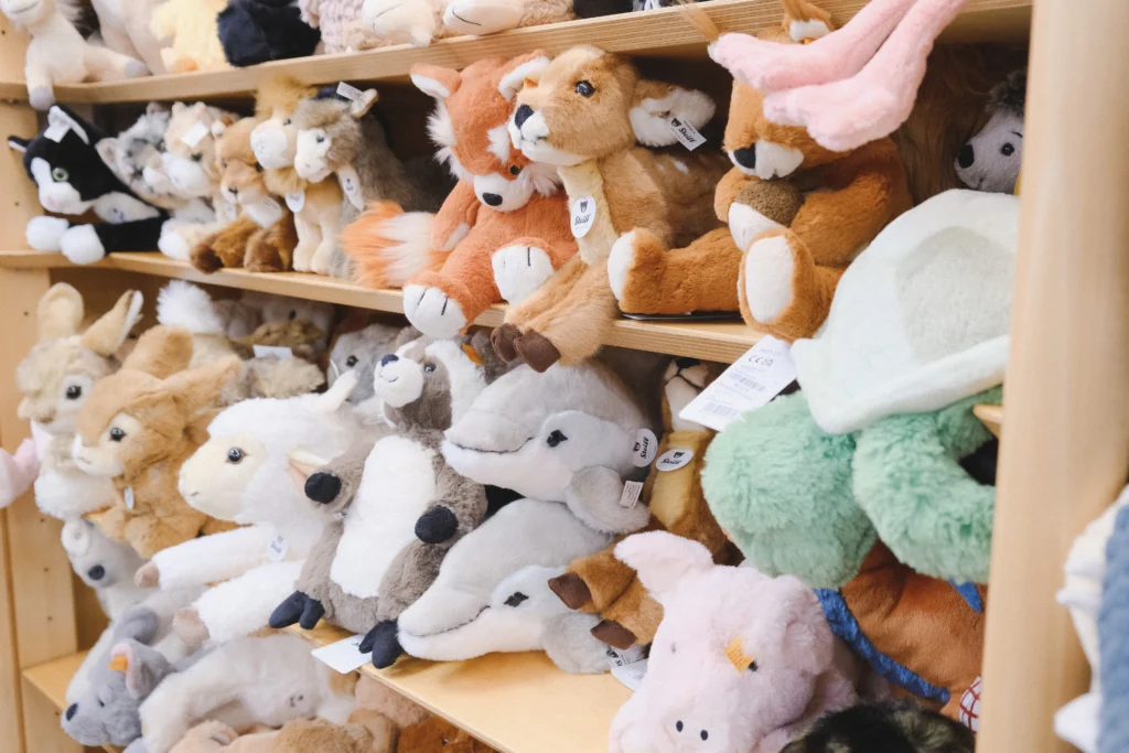 Mehrere Holzregale sind dicht mit Kuscheltieren unterschiedlichster Tierarten gefüllt, darunter Füchse, Rehe, Delfine und weitere Plüschfiguren in verschiedenen Größen.