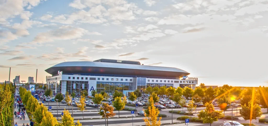 Außenansicht der SAP Arena Mannheim mit Parkplätzen und Bäumen im Vordergrund bei Sonnenuntergang.
