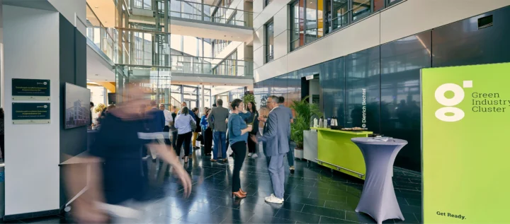 People are standing and moving through the bright lobby of a modern office building during a networking or corporate event.