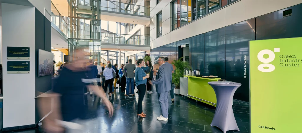Menschen stehen und bewegen sich in der hellen Eingangshalle eines modernen Bürogebäudes während einer Netzwerk- oder Unternehmensveranstaltung.