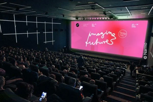 Blick auf die Leinwand in einem vollbesetzten Kinosaal, auf der in weißer Farbe "Imagine Futures" auf pinkem Hintergrund steht